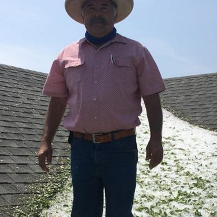 Man in cowboy hat on hail-covered roof. He wears jeans, a red shirt, and a brown belt.