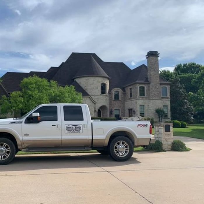 White pickup truck parked in front of a large stone house.