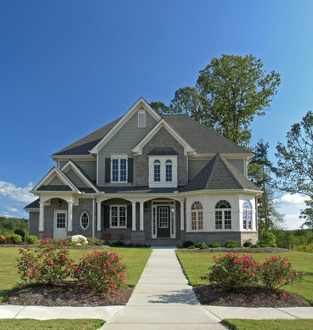 Two-story house with gray and brick facade, front porch, and manicured lawn under a blue sky.