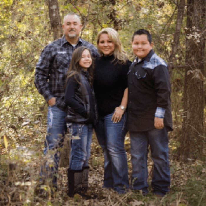 Family of four posing outdoors among trees. They wear jeans and jackets, smiling.